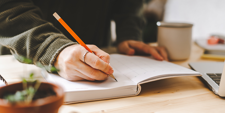 A person taking notes next to a laptop